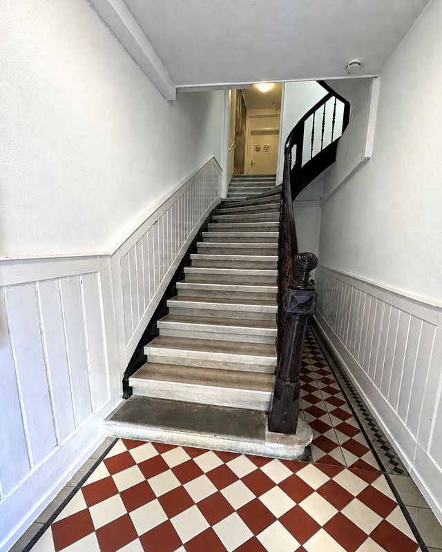 Eingangsbereich mit historischer Holztreppe und rot-weißem Fliesenboden